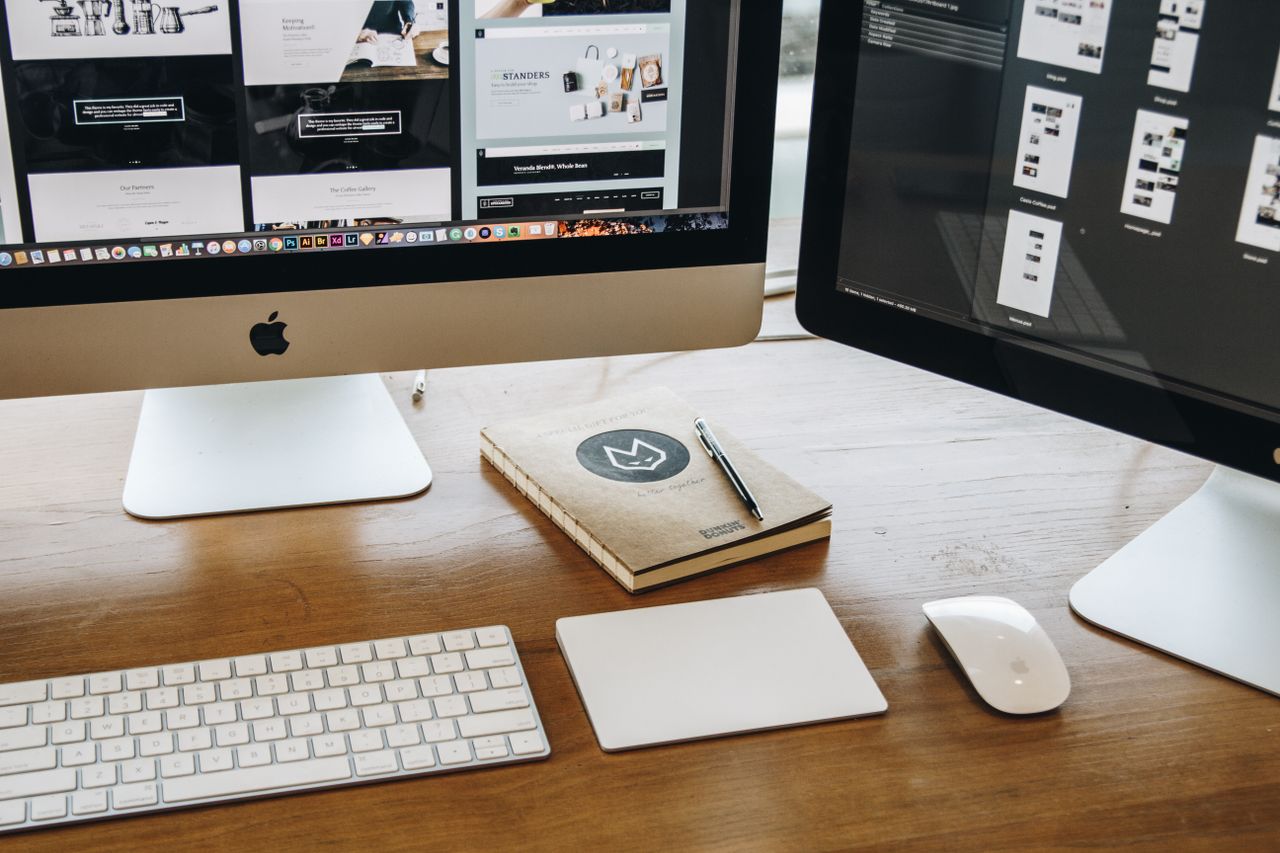 An uncluttered desk arrangement with two monitors, a keyboard, mouse, and notebook designed for efficient work.